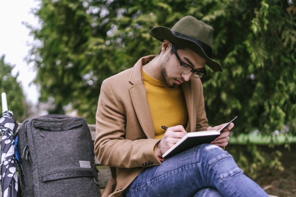 man writing in journal in a park