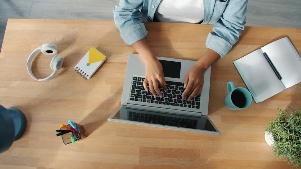 Top-down view of a person working on a laptop at a neat desk with accessories.