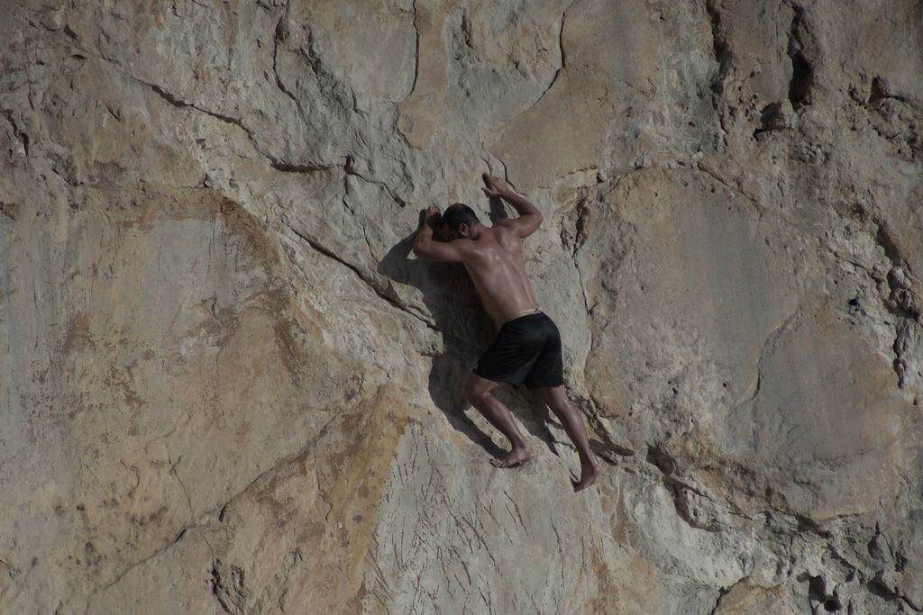 Athletic man engaged in rock climbing on a natural cliff face under sunlight.